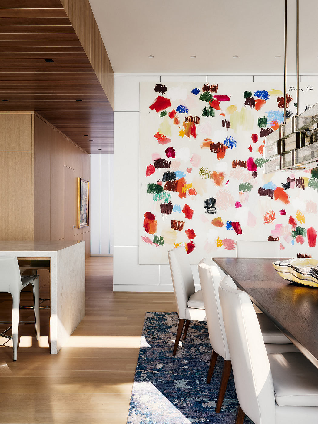 Vibrant abstract artwork adorns the modern, minimalist dining room with wooden accents.