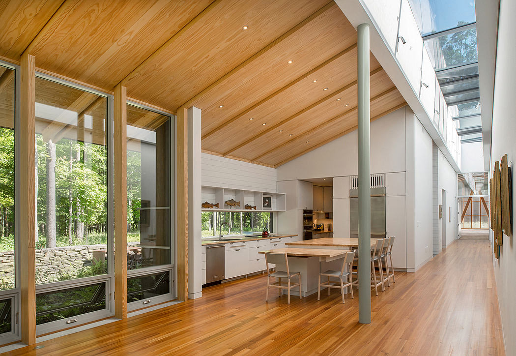 Spacious modern kitchen with wood-paneled ceiling, large windows overlooking nature.