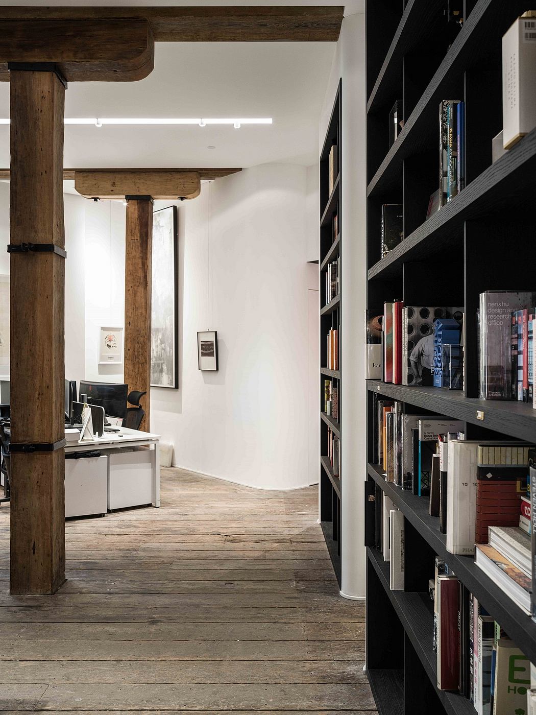 A spacious, modern interior with exposed wooden beams, bookshelves, and a minimalist workspace.