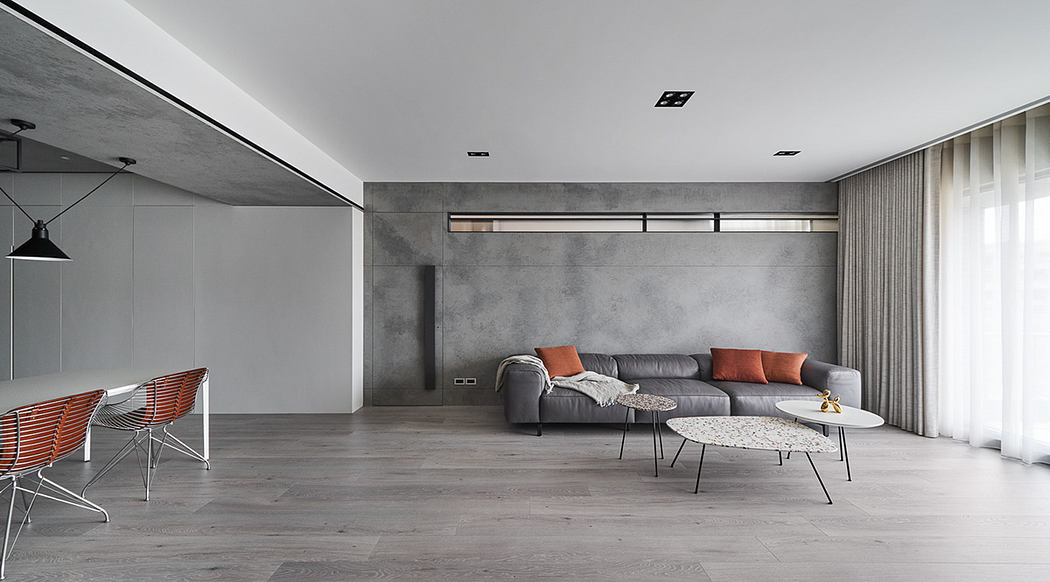 Modern, minimalist living room with concrete walls, gray sofa, and abstract coffee tables.