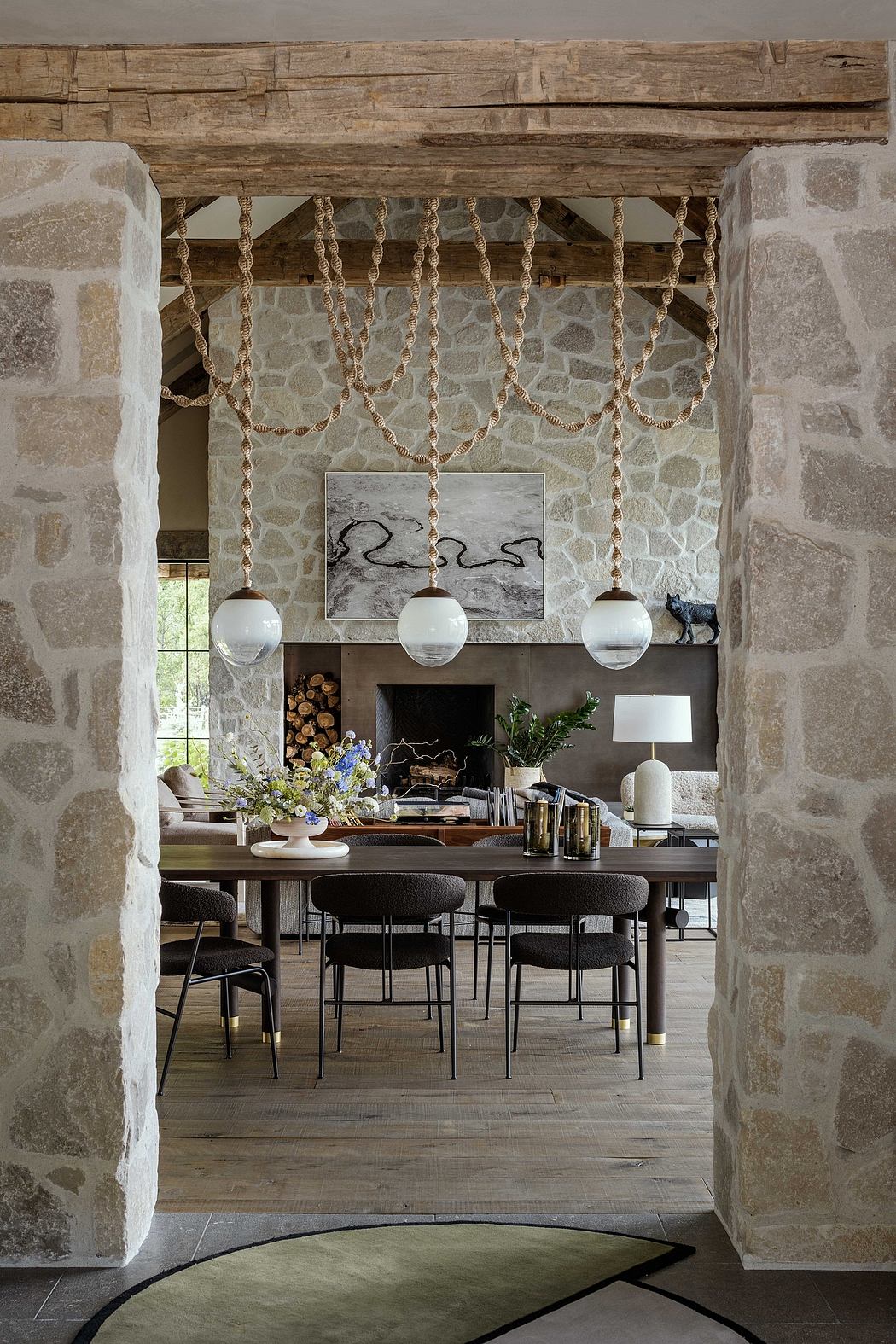 Rustic stone walls frame a modern dining space with pendant lights, wooden beams, and a marble fireplace.
