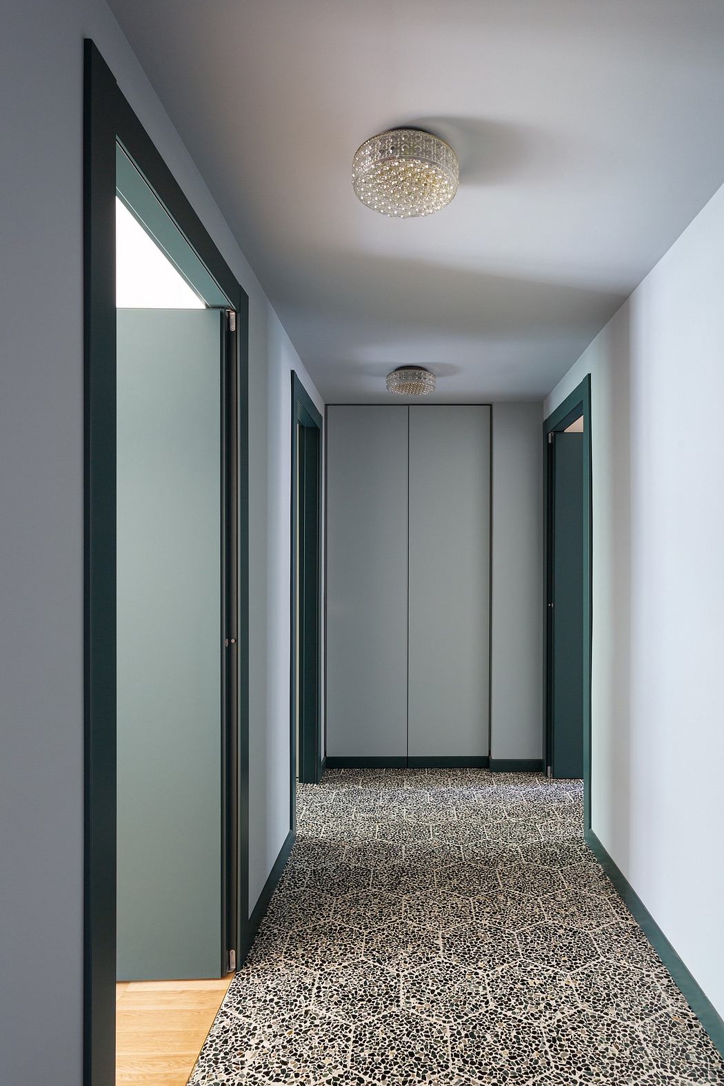 A sleek, modern hallway with a terrazzo floor, glass panels, and crystal chandeliers.