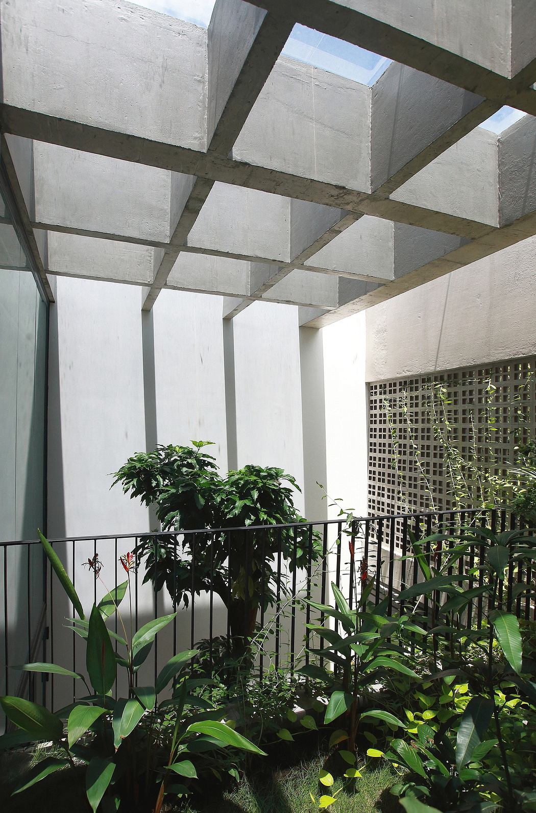 A modern greenhouse-like structure with concrete beams and lush foliage.