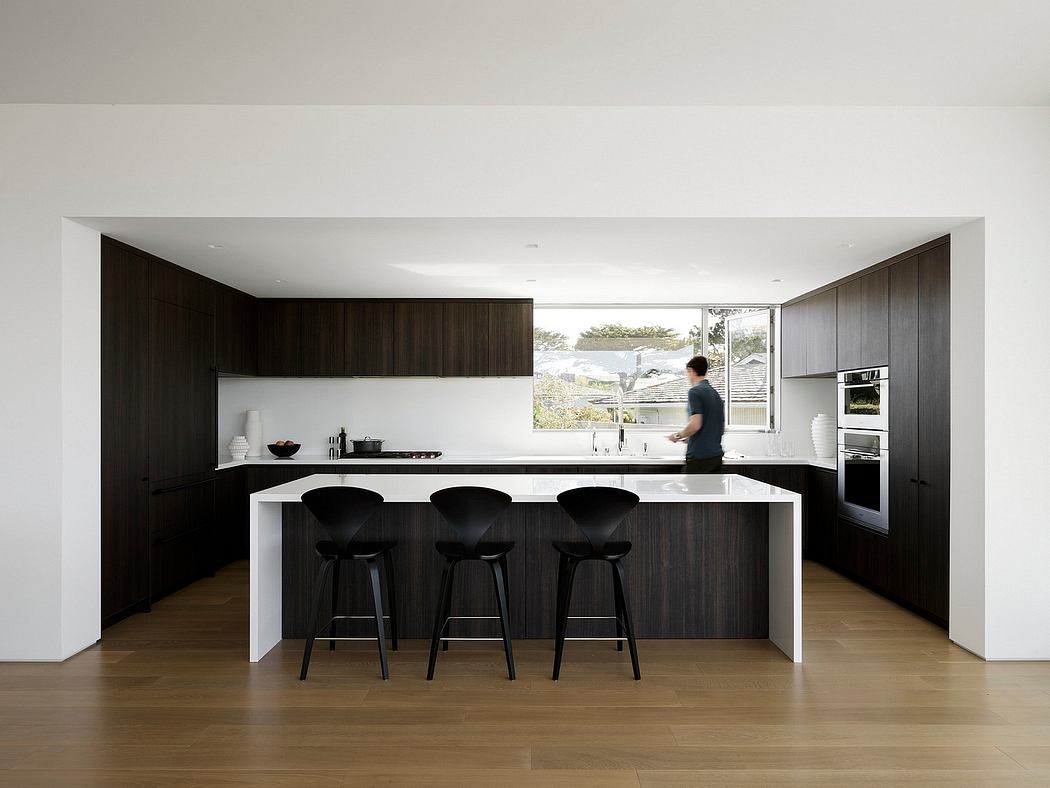 Sleek, modern kitchen with dark wood cabinets, white countertops, and black barstools. Large window provides natural light.