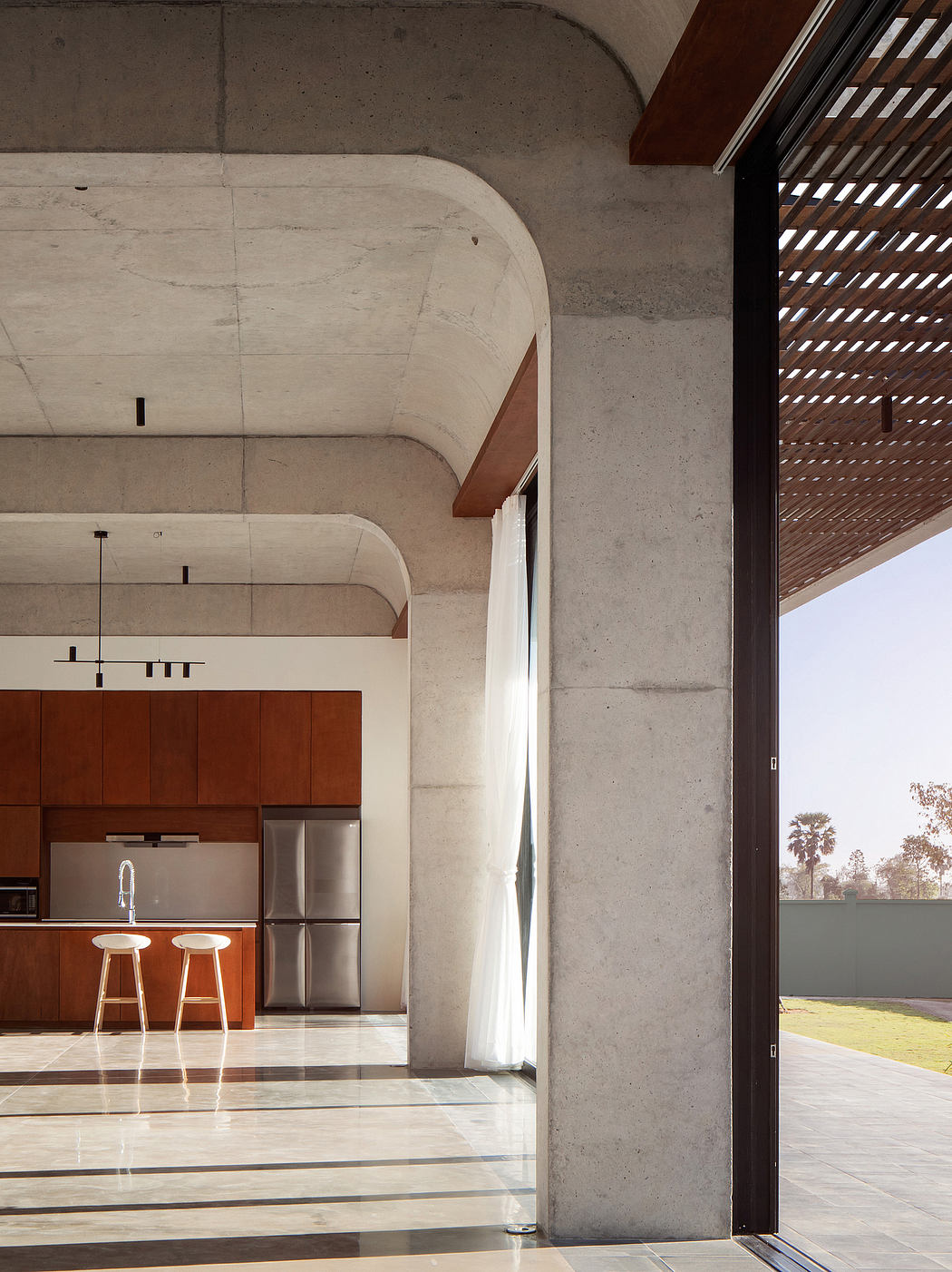 Modern kitchen with concrete arches, wood cabinets, and glass sliding door to outdoor view.