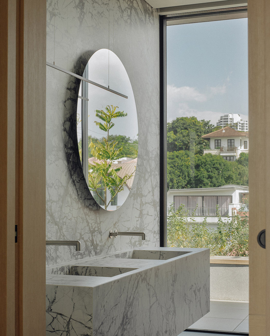 Elegant bathroom with marble vanities, oval mirror, and lush garden view.