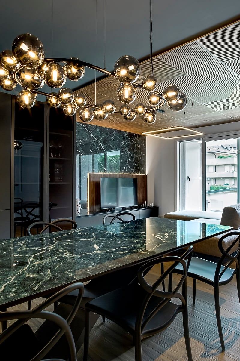 A modern dining room with a sleek marble table, metallic globe pendant lights, and a TV console.