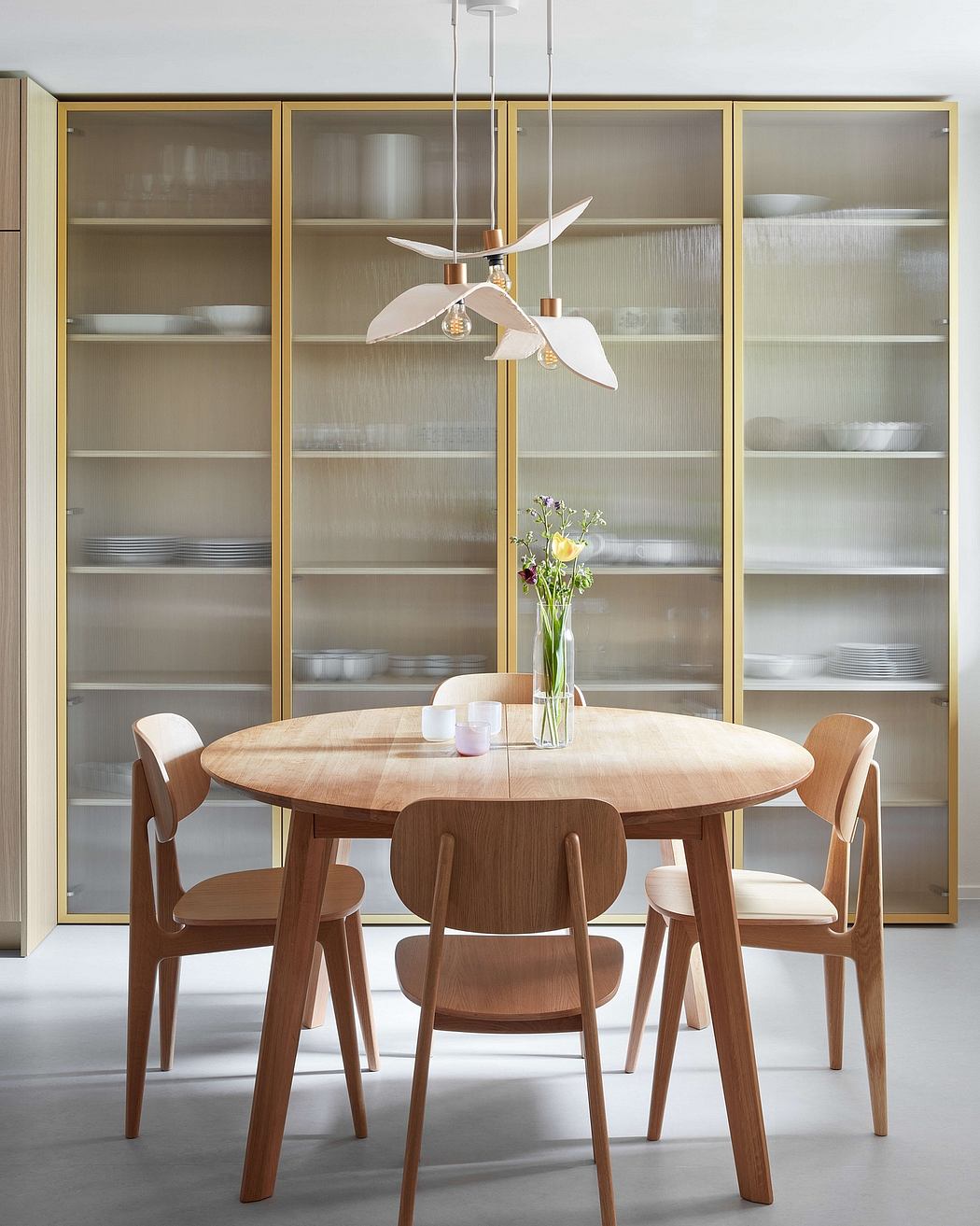Modern dining room with wooden table, chairs, and glass-front cabinets displaying plates.