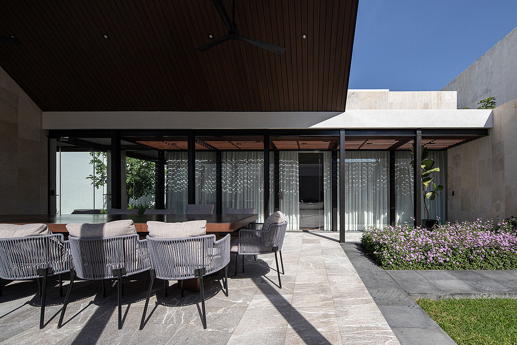 Minimalist outdoor dining area with glass walls, wooden beams, and stone flooring.