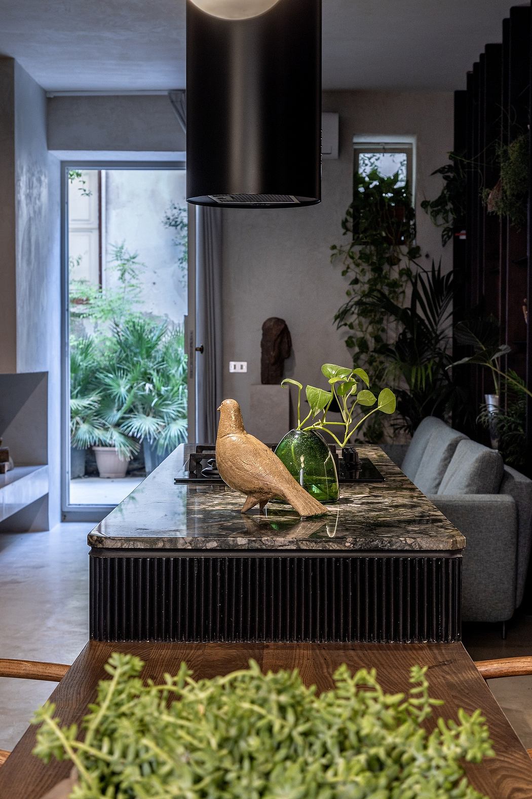 A modern, minimalist living room with a striking wood and metal coffee table, potted plants, and a window view.