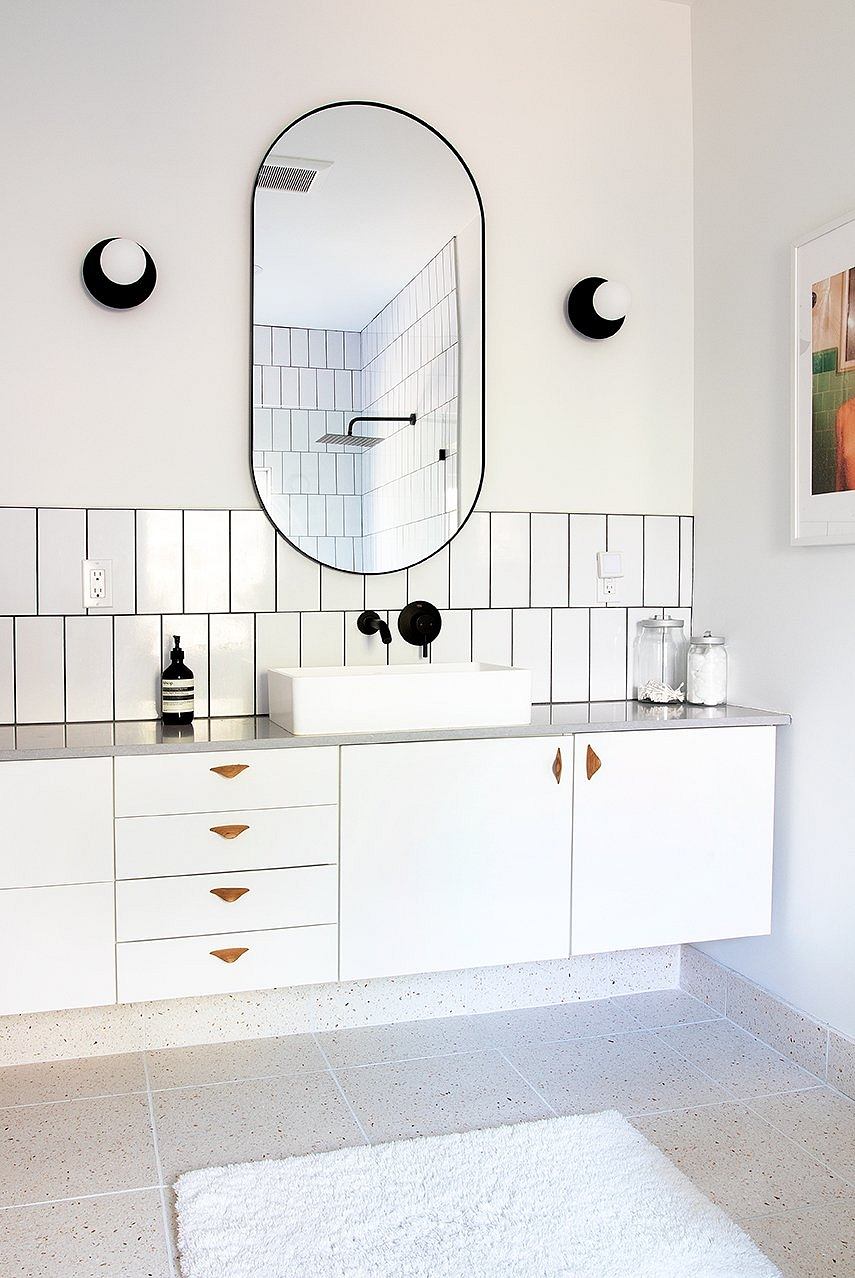 Minimalist bathroom design with large oval mirror, white cabinets, and terrazzo tiles.