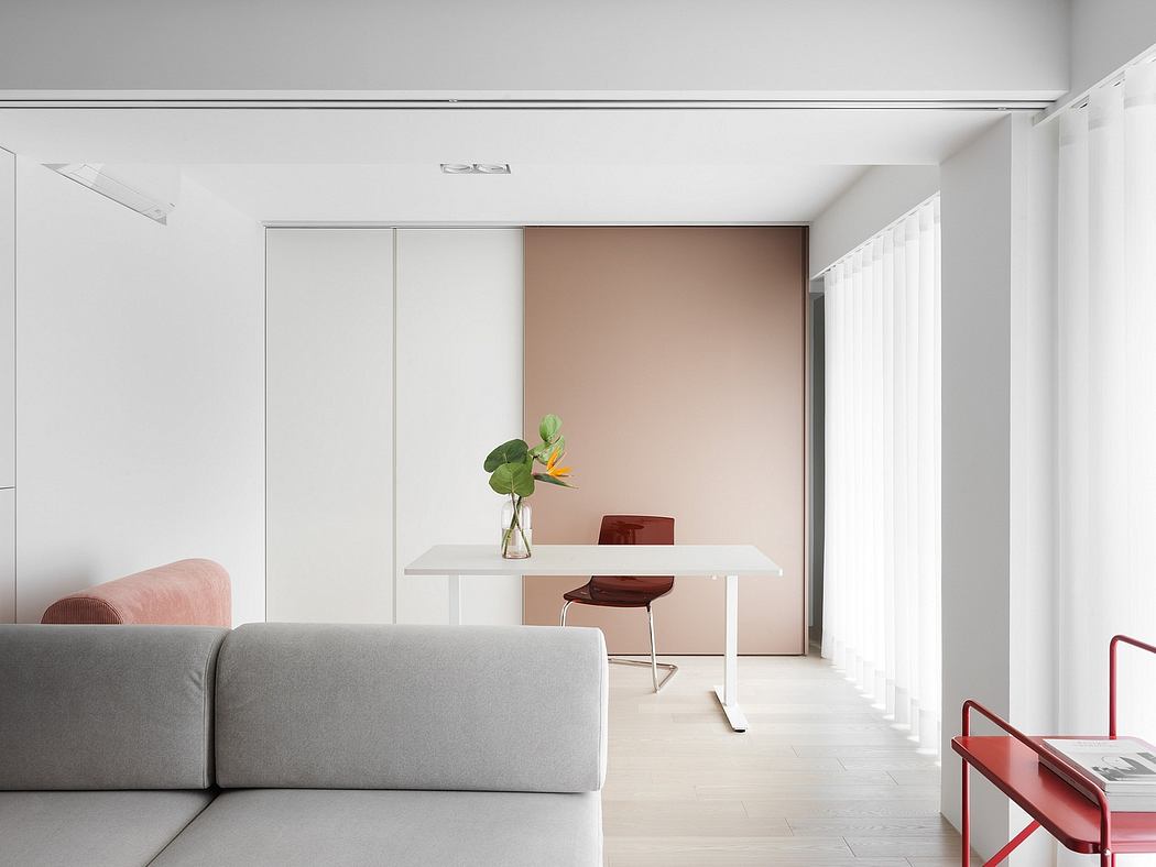 A minimalist living room with neutral-colored furniture and a compact desk setup in the background.