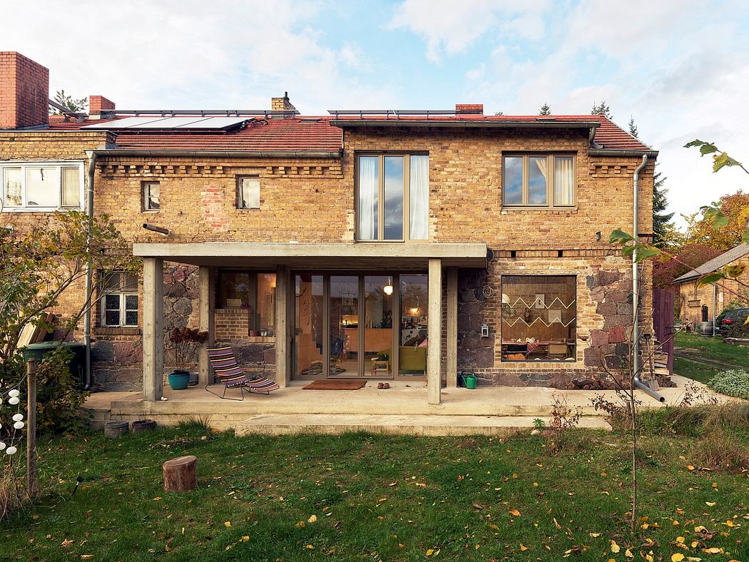 A brick and stone house with a covered patio, large windows, and a surrounding grassy yard.