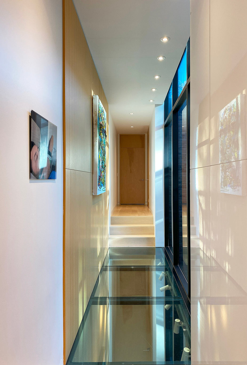 Sleek, modern hallway with glass floor, recessed lighting, and colorful artwork.
