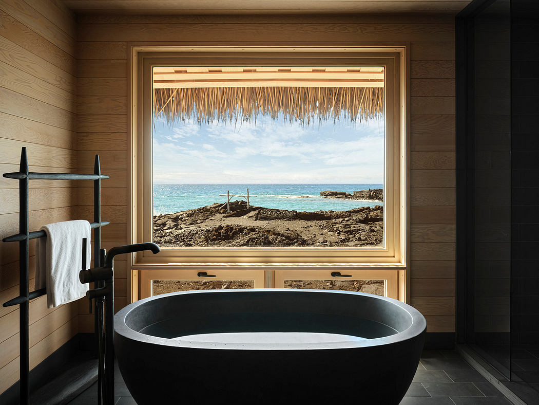Rustic bathroom with an oval tub and panoramic view of the ocean framed by a thatched roof.