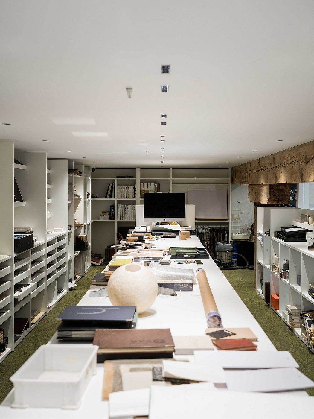 A cluttered, modern workspace with built-in shelving, numerous books, and various electronic devices.