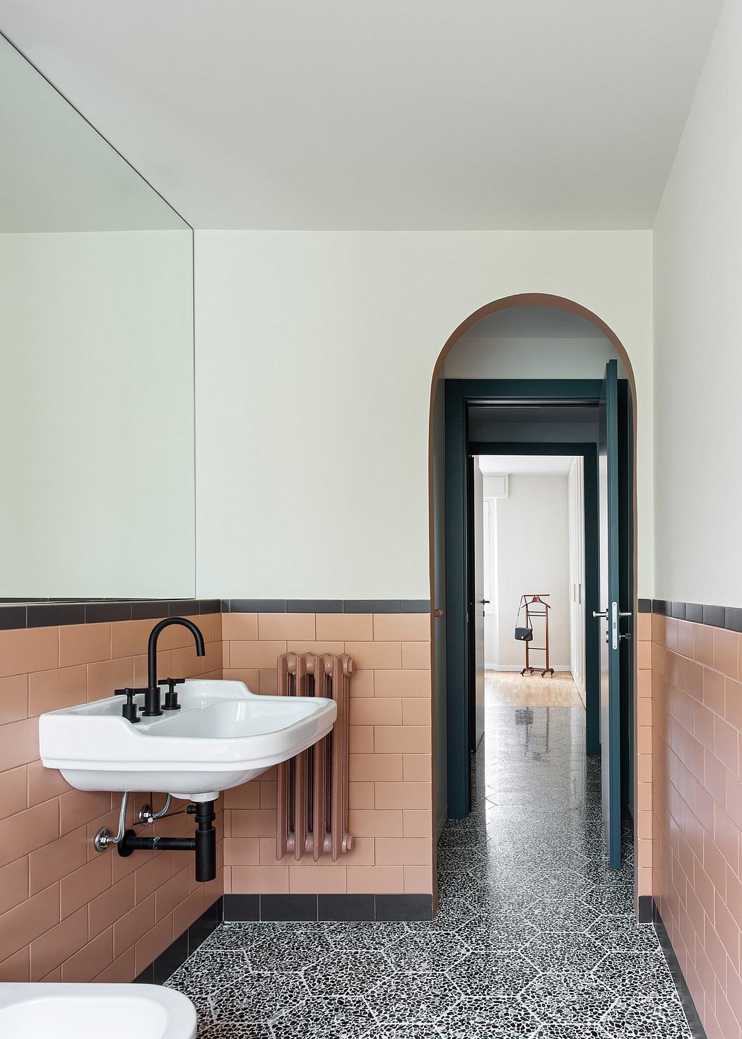 An interior design with a stylish bathroom featuring pink tiles, an arched doorway, and terrazzo flooring.