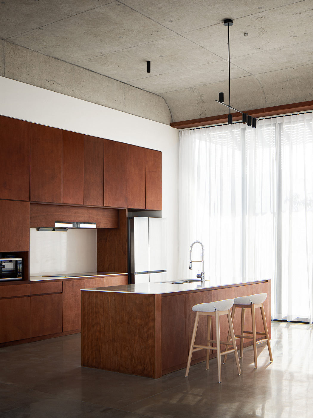 A modern kitchen with a sleek wooden cabinetry, concrete ceiling, and minimalist lighting.