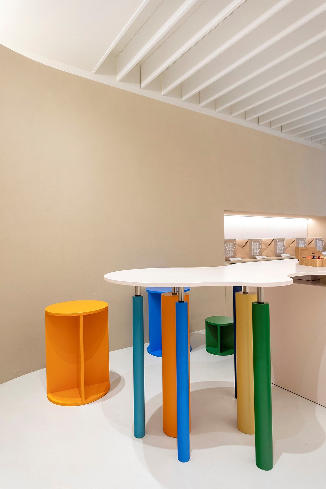 Modern interior with colorful geometric stools and white oval table. Beige walls and wooden ceiling beams.