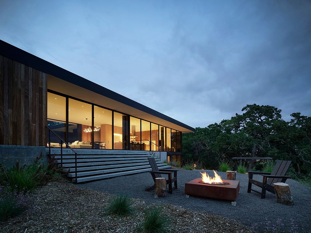 A modern wooden and glass home with a fire pit and outdoor seating area at dusk.