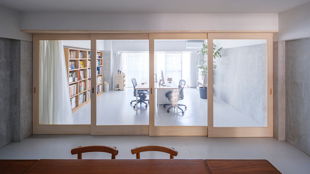Minimalist home office with large sliding glass doors, wooden shelves, and a sleek table.