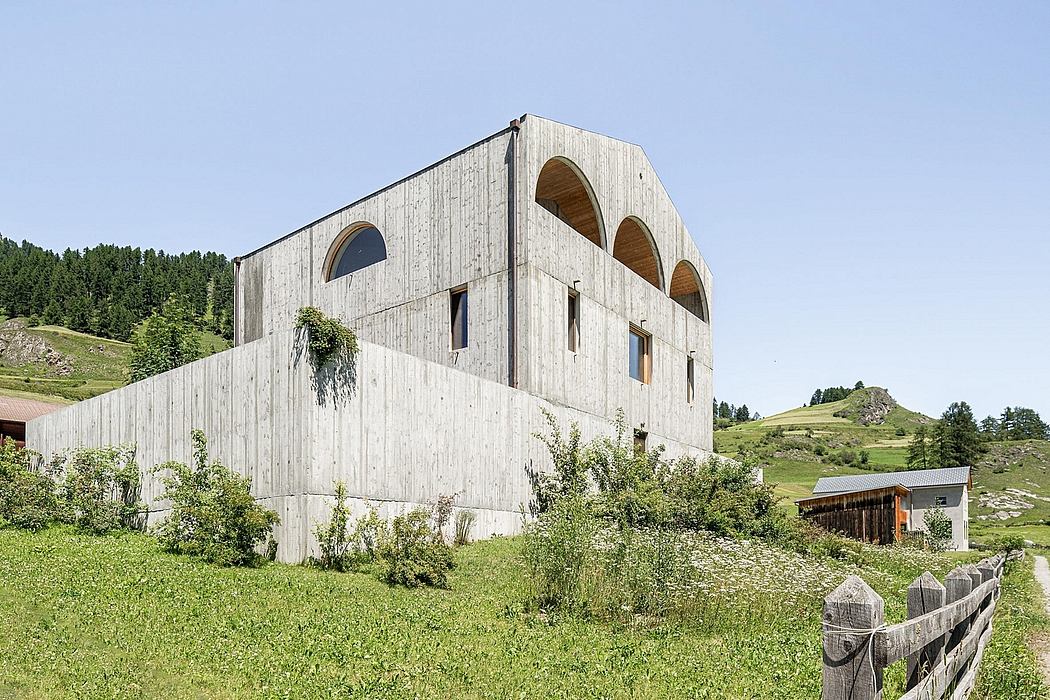 Striking concrete structure with arched windows in a verdant rural setting.