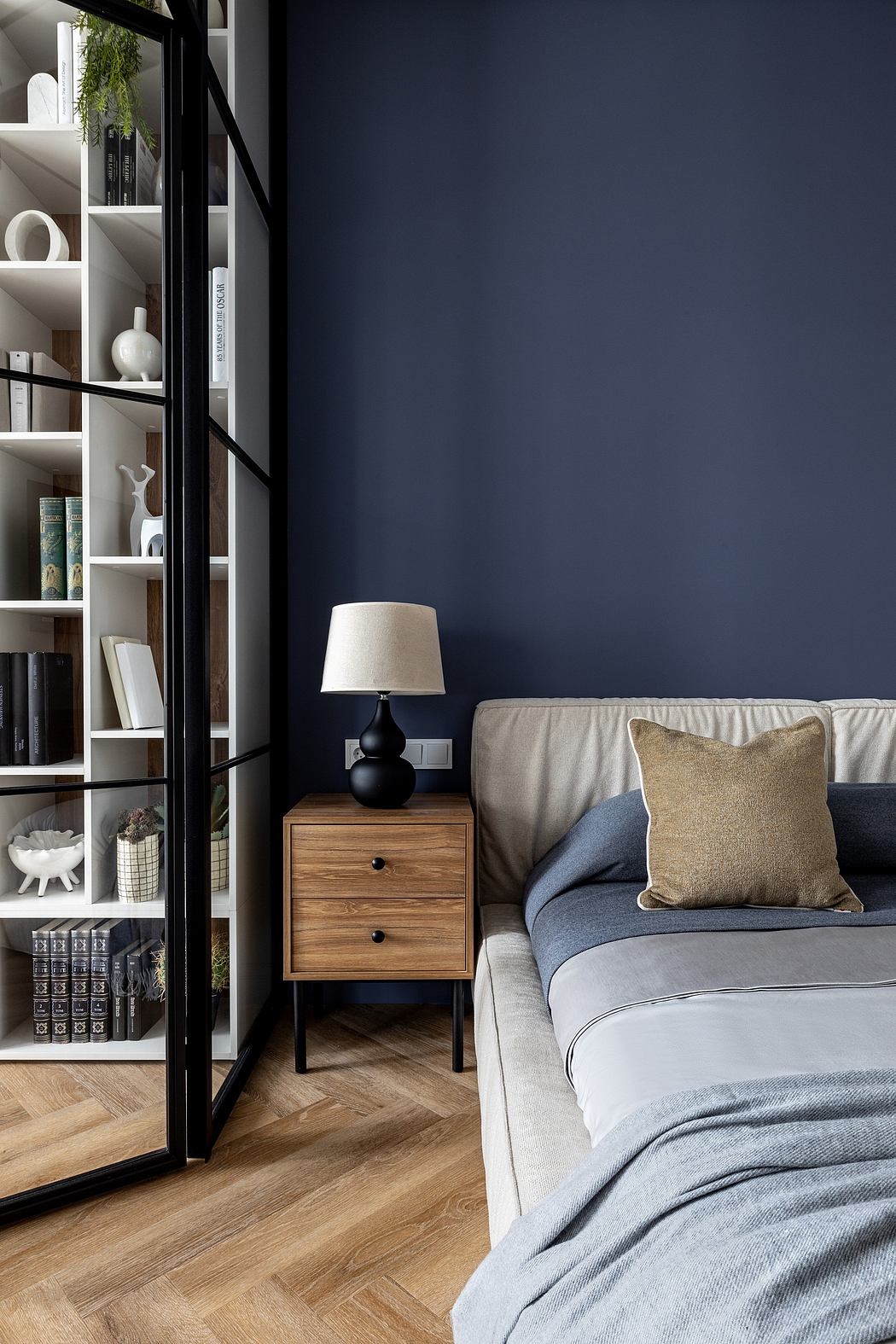 Cozy bedroom with dark-colored walls, wooden nightstand, and shelving unit displaying decor.
