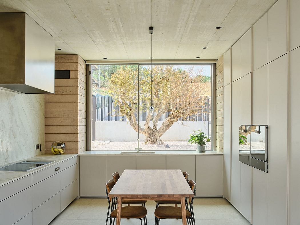 A modern kitchen and dining area with a large window overlooking a tree-filled yard.