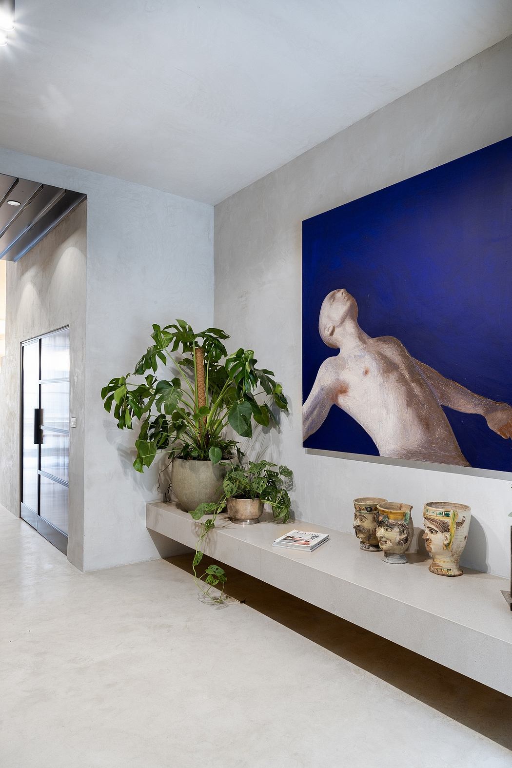 A modern interior with a vibrant blue wall, a stone sculpture, and lush greenery.