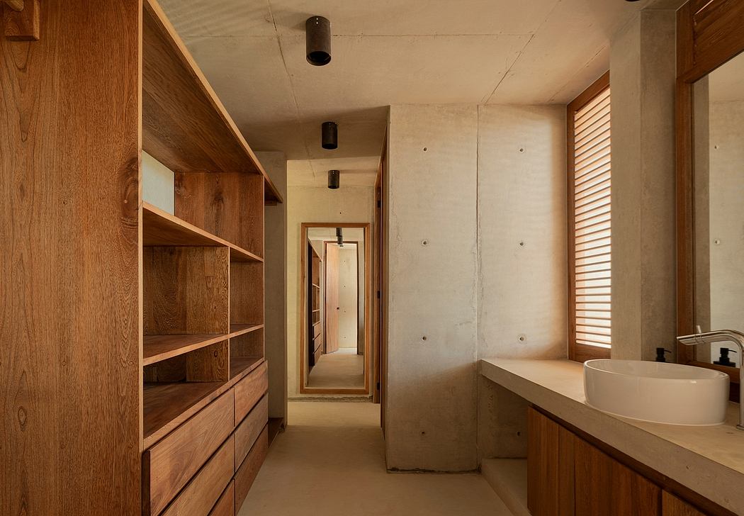 A long narrow hallway with wooden shelves and a bathroom with a vessel sink at the end.