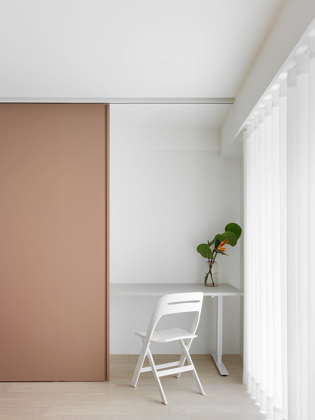 A simple, minimalist workspace with a beige sliding door, white chair, and potted plant.
