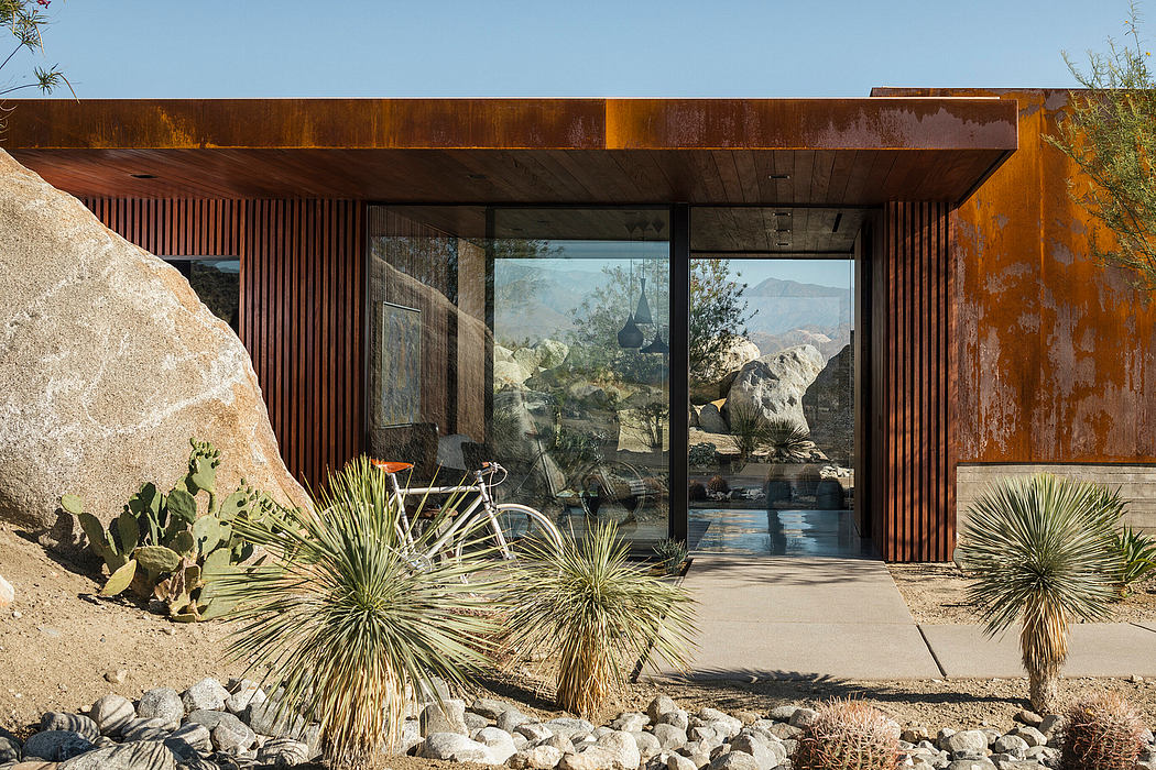 A modern desert home with a bold, rusty exterior and large glass windows overlooking the landscape.
