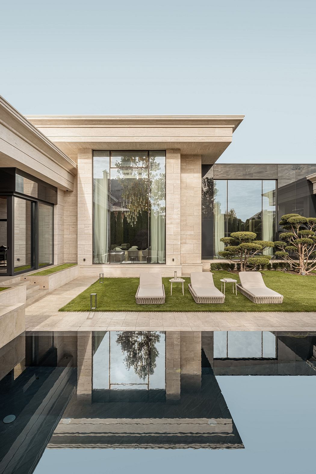 Elegant modern exterior with sculptural landscaping, reflecting pool, and glass walls.