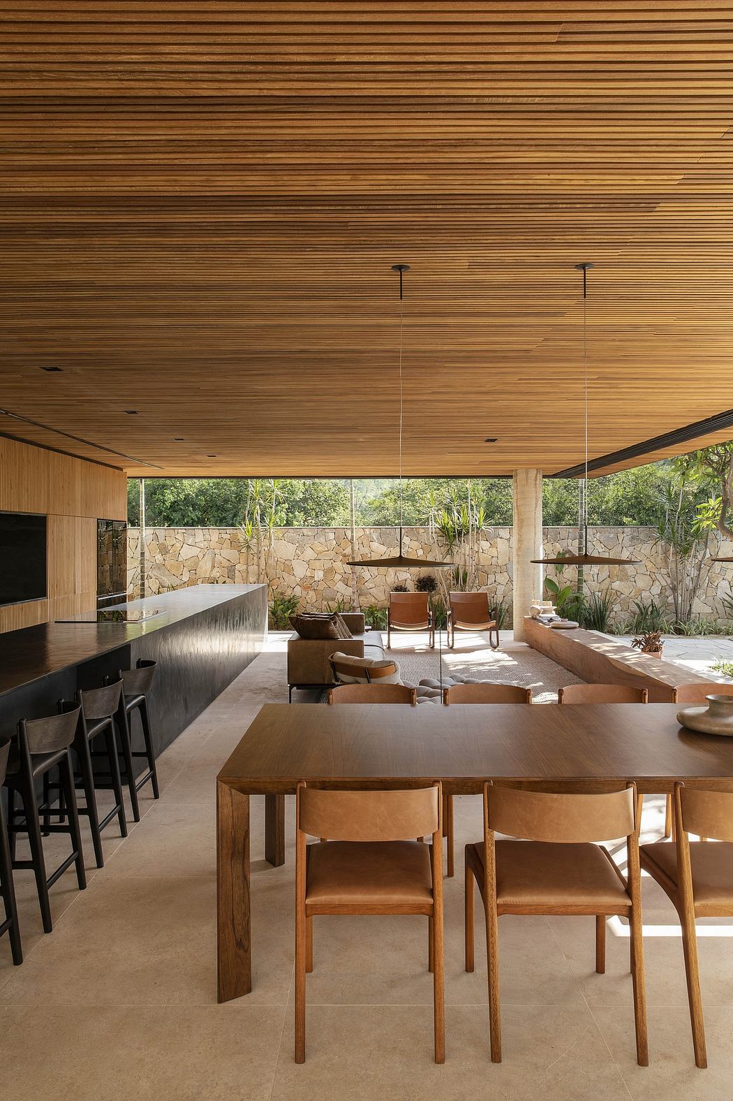 Expansive indoor-outdoor living space with wooden beams, stone walls, and minimalist furnishings.