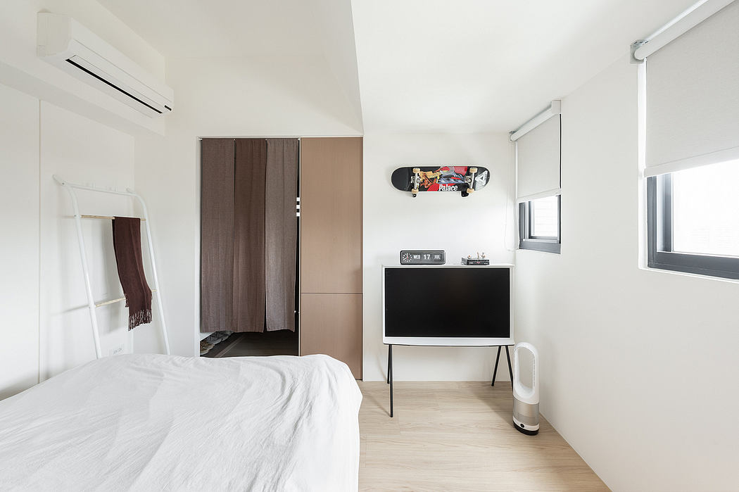 A minimalist bedroom with a built-in closet, TV stand, and a skateboard decorating the wall.