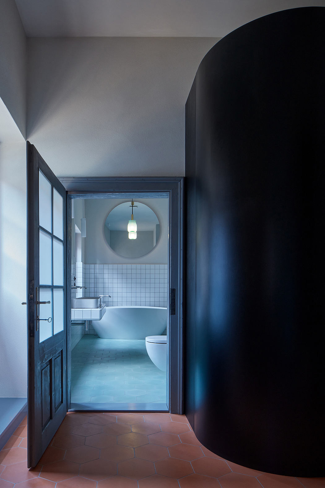 A moody, circular archway leads to a minimalist, tiled bathroom with geometric flooring.