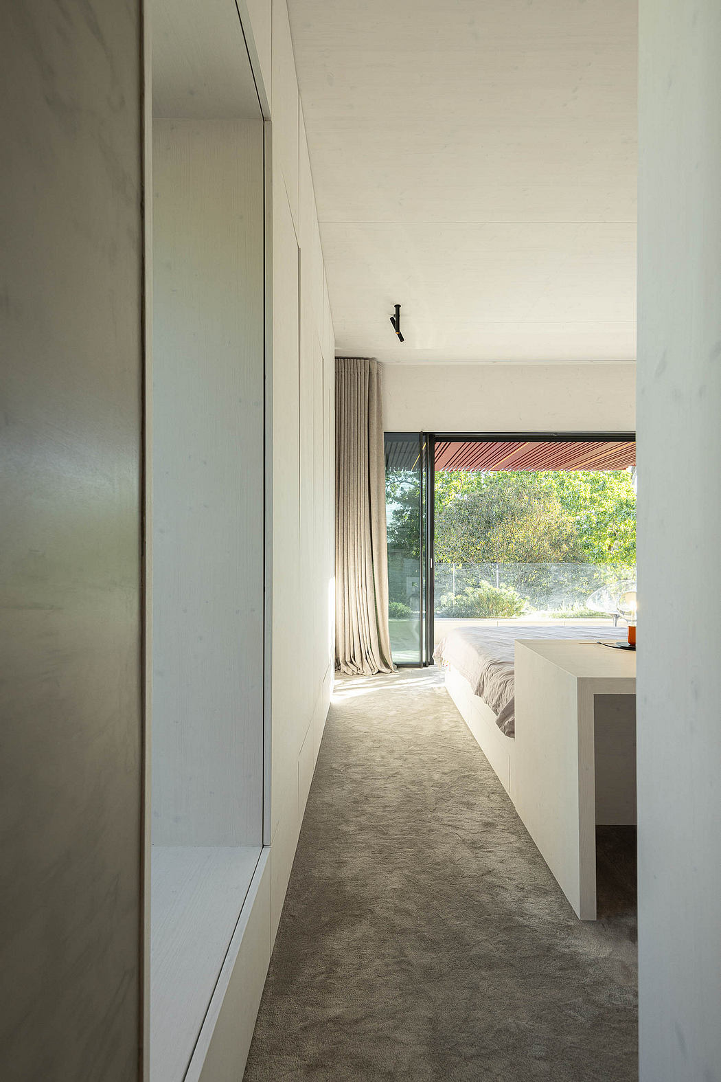 Expansive bedroom with floor-to-ceiling window, sleek built-in cabinetry, and subtle lighting.