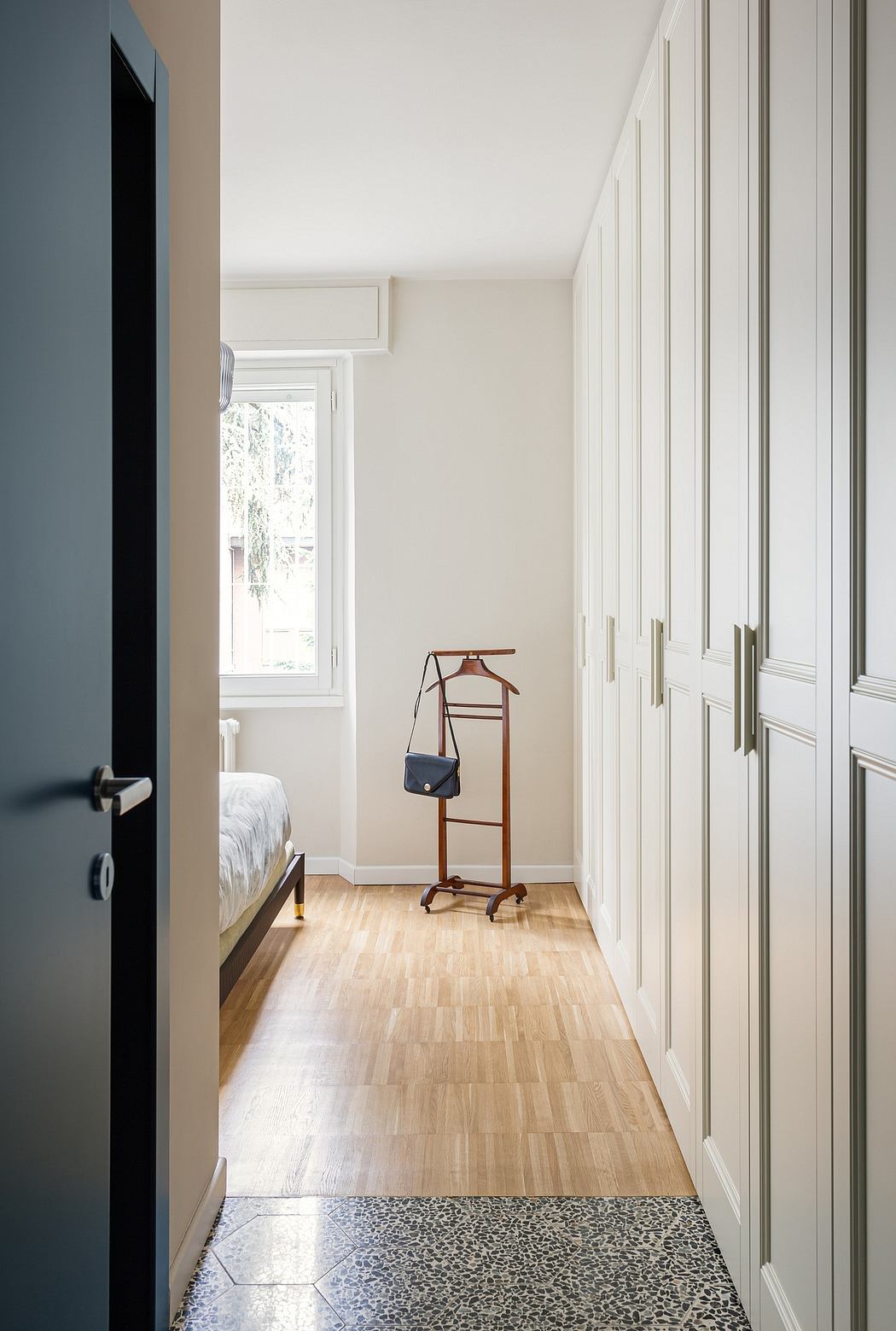 Bright, minimalist bedroom with clean lines, built-in closets, and a wooden clothing rack.