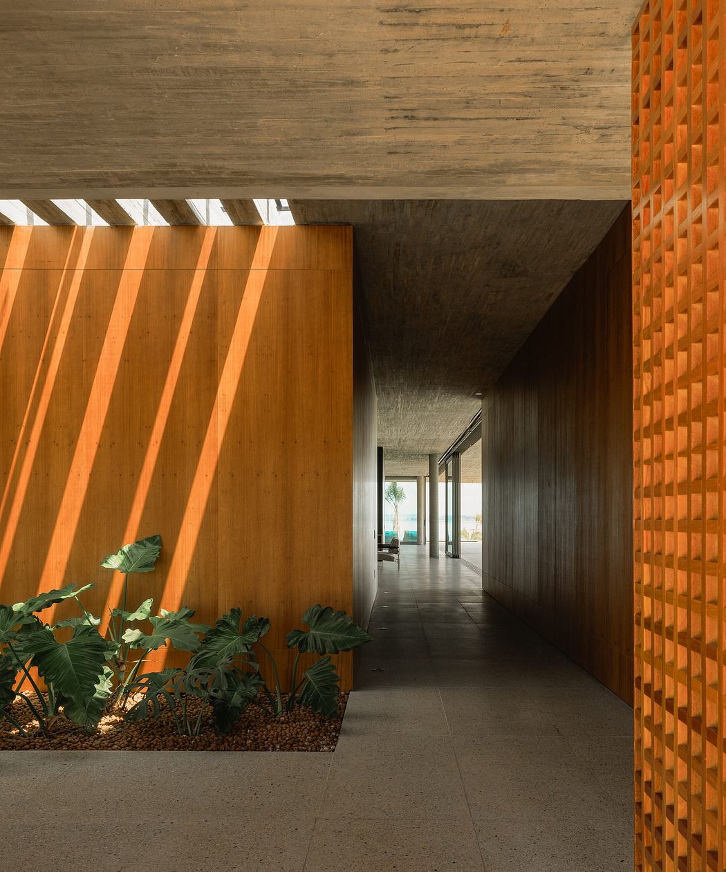 An architectural corridor with a concrete ceiling, wooden paneling, and lush tropical greenery.