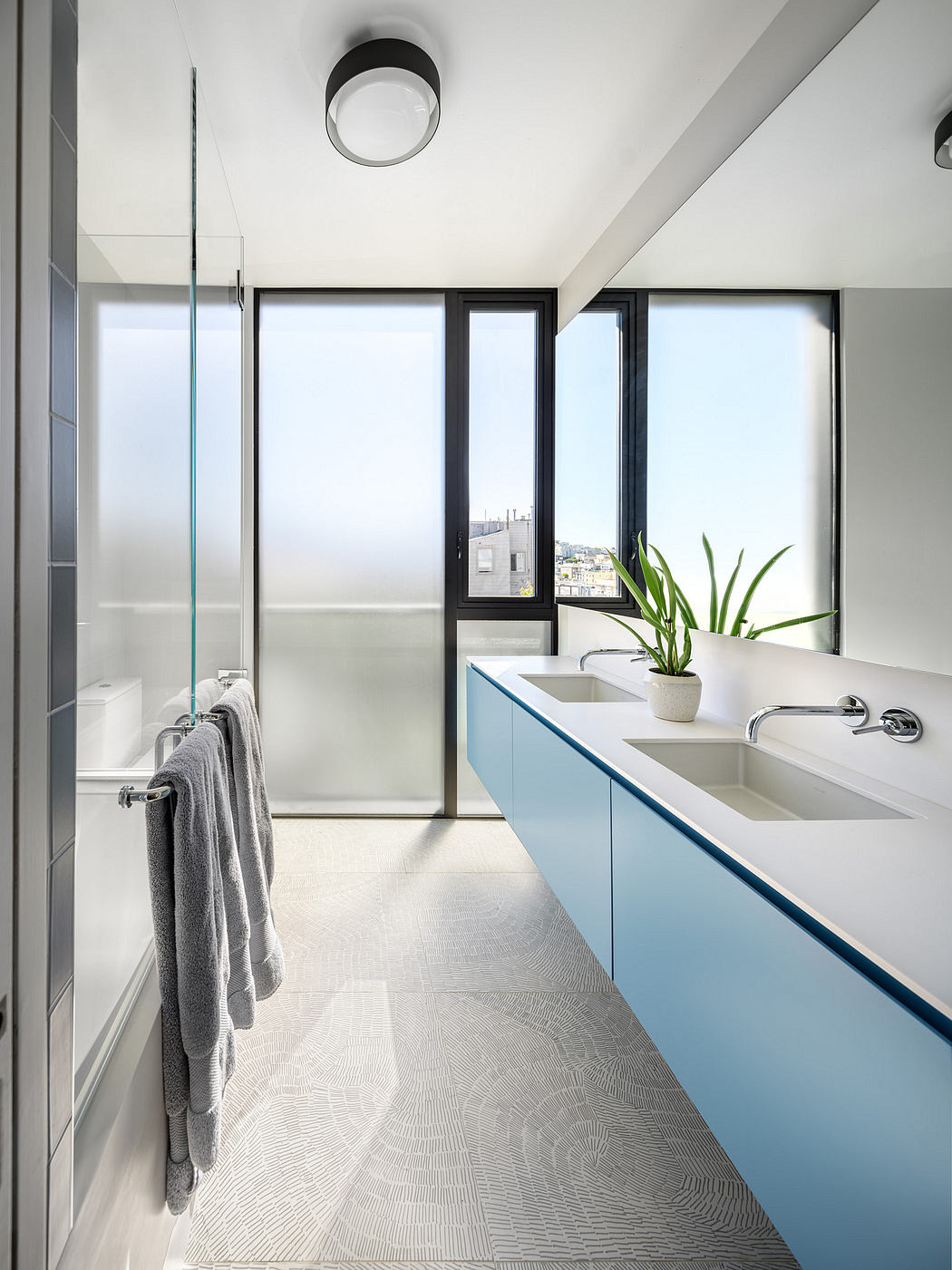 Contemporary bathroom with minimalist design, large windows, blue vanity, and patterned tile flooring.