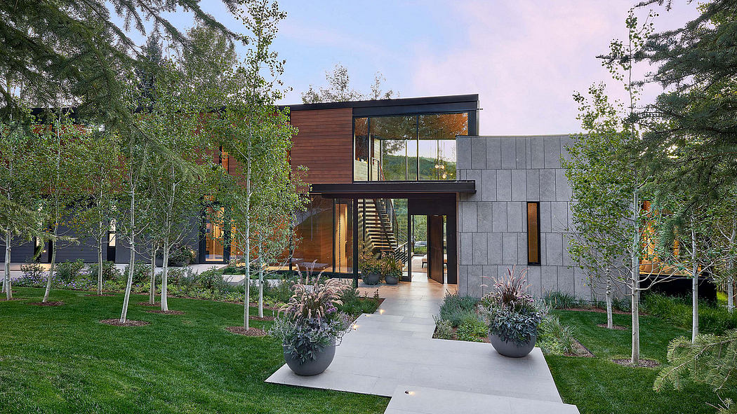 A modern, two-story home with glass walls, wood siding, and a concrete exterior, surrounded by lush greenery.