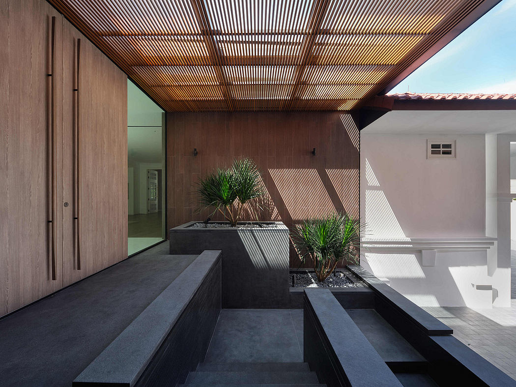 Sleek modern entrance with wooden slatted ceiling, dark stone benches, and potted plants.