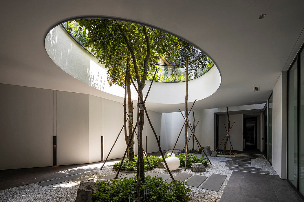 Minimalist indoor garden with curved skylight, tree trunks, and gravel path.