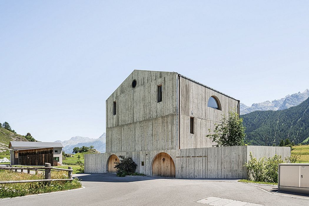 A modern, angular wooden building with arched entryways, set against a mountainous backdrop.