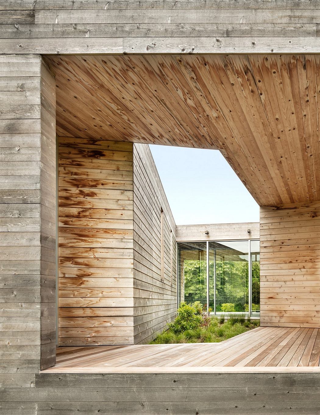 A modern wooden structure with a large glass window overlooking a lush, green landscape.
