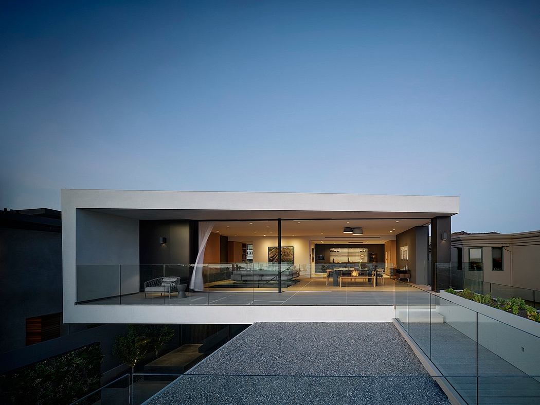 A modern, minimalist house with large glass windows, an open floor plan, and a gravel patio.