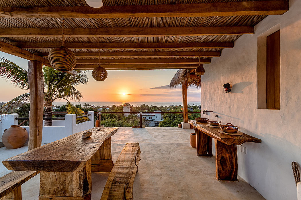 Rustic outdoor dining area with wooden beams, hanging lights, and stunning ocean view.