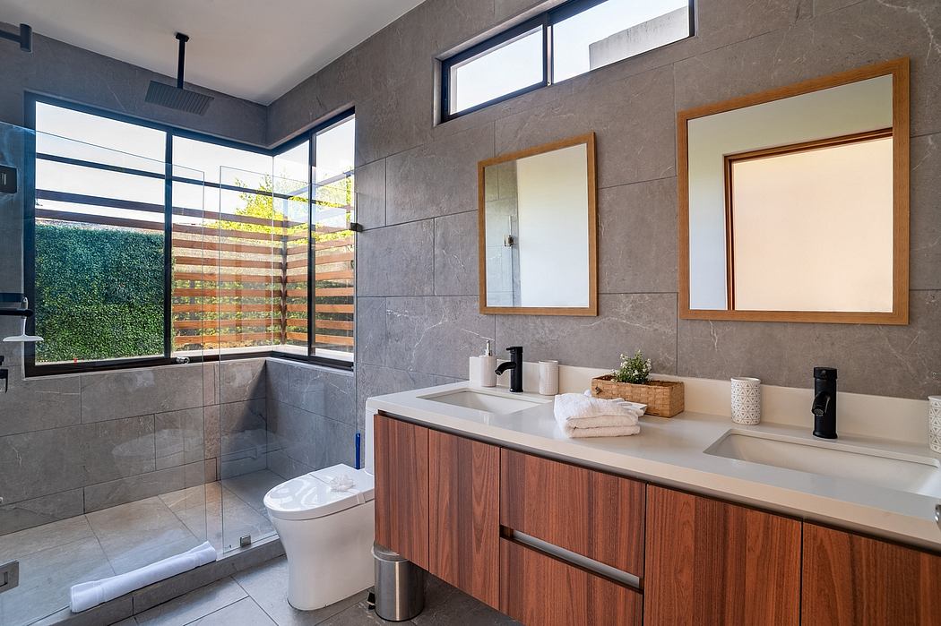 Modern bathroom with wooden vanity, gray tile walls, and large windows offering natural light.