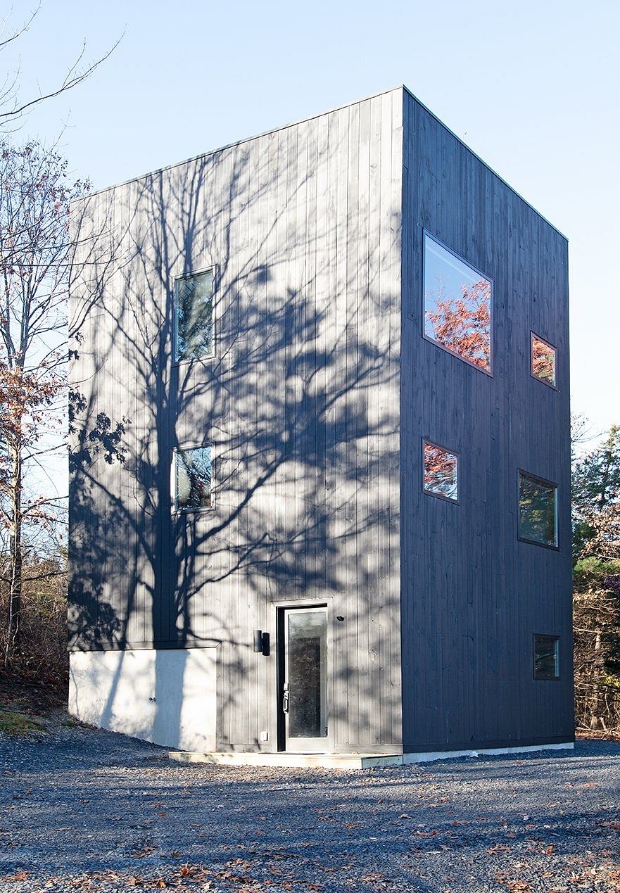 A modern, rectangular building with a wooden exterior and strategically placed windows, standing in a natural setting.