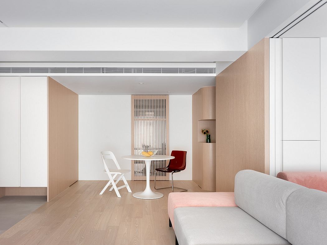 Minimalist apartment with white walls, wooden furnishings, and a central dining area.